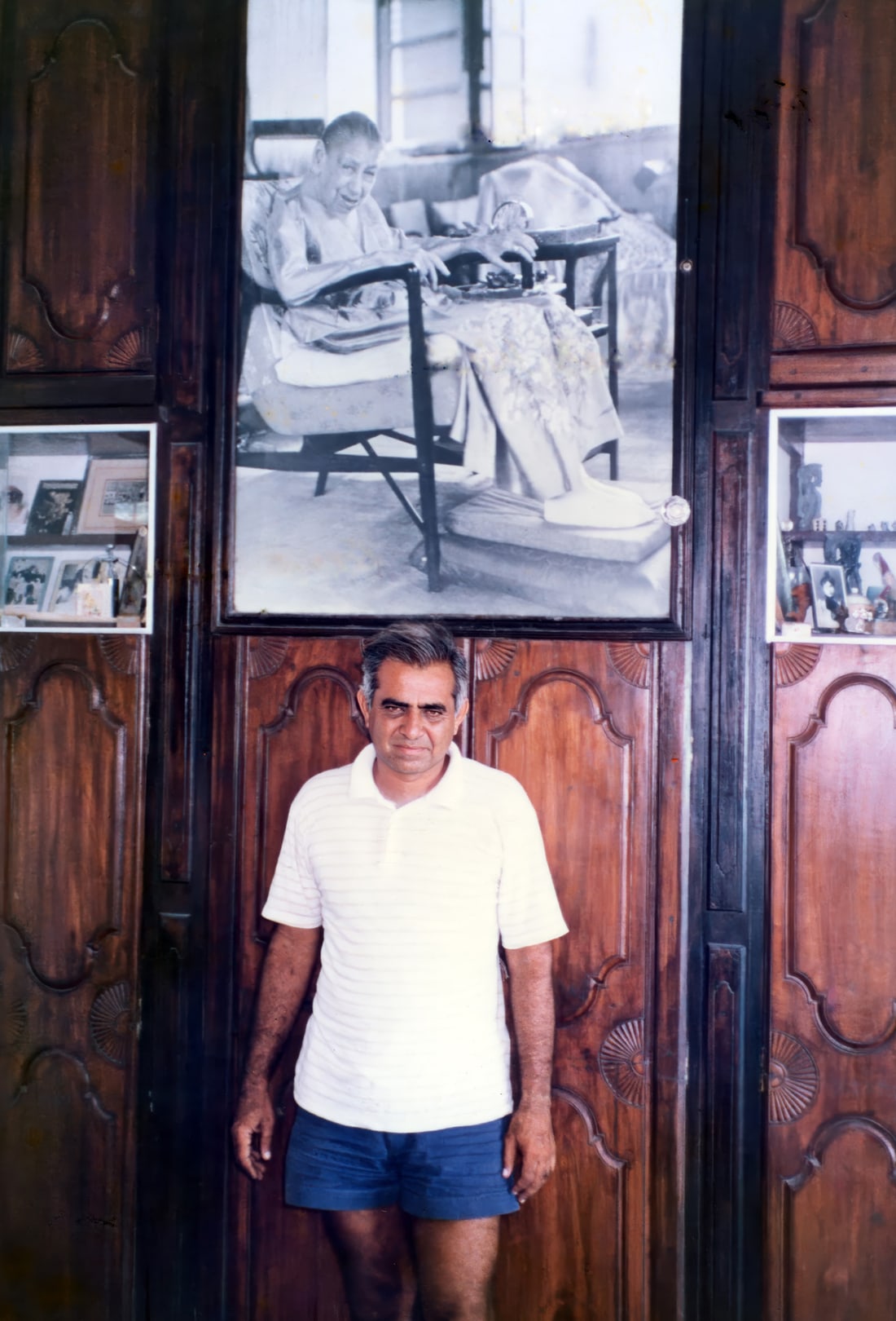 Promesse standing in his home beneath a large framed photograph of the Mother
